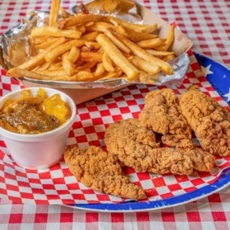 Crispy chicken tenders, golden fries in foil, and a side of peach cobbler on a checkered tray.