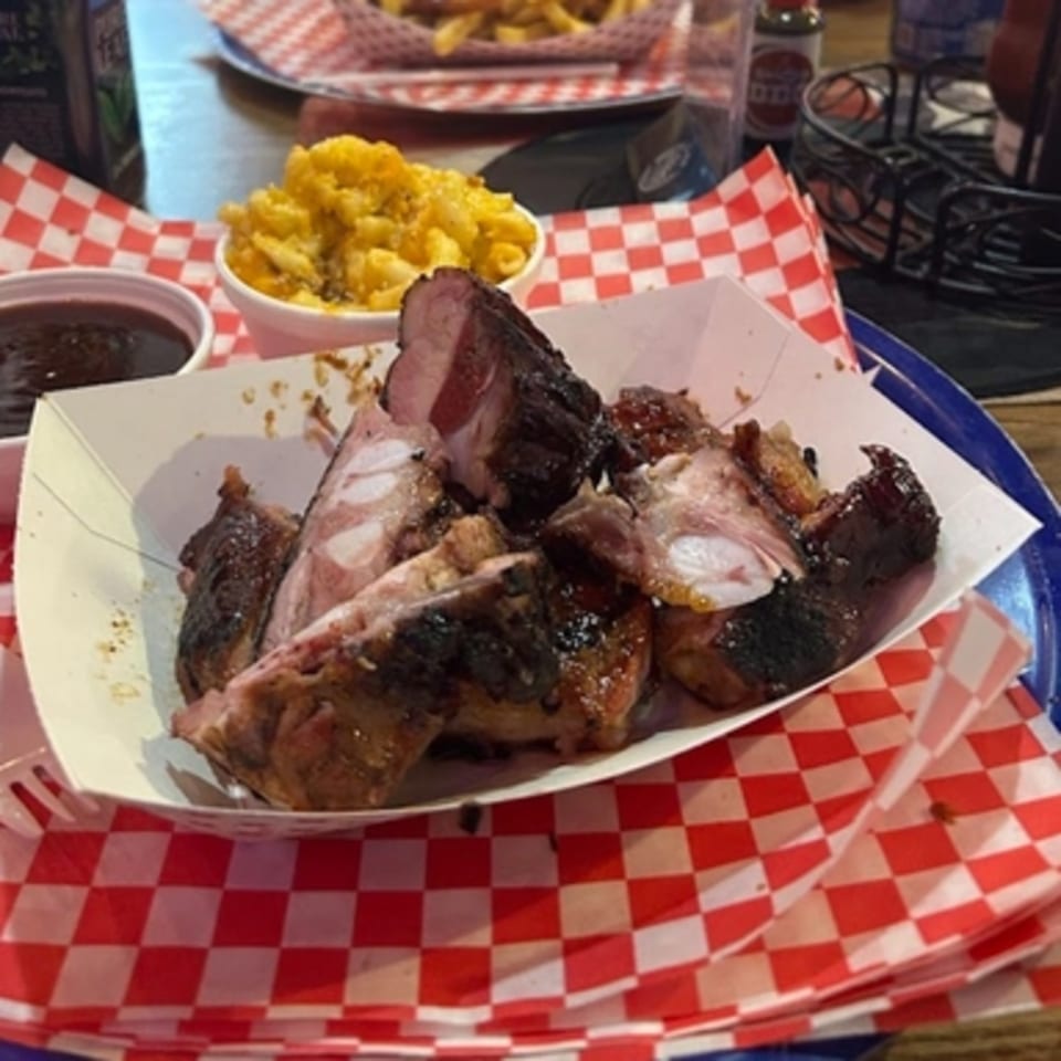 Real Smoq’ed BBQ ribs, mac and cheese, and barbecue sauce on a red and white checkered tray.