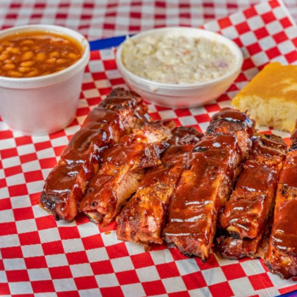 Real Smoq’ed BBQ ribs with baked beans, coleslaw, and cornbread on a red and white checkered tray.