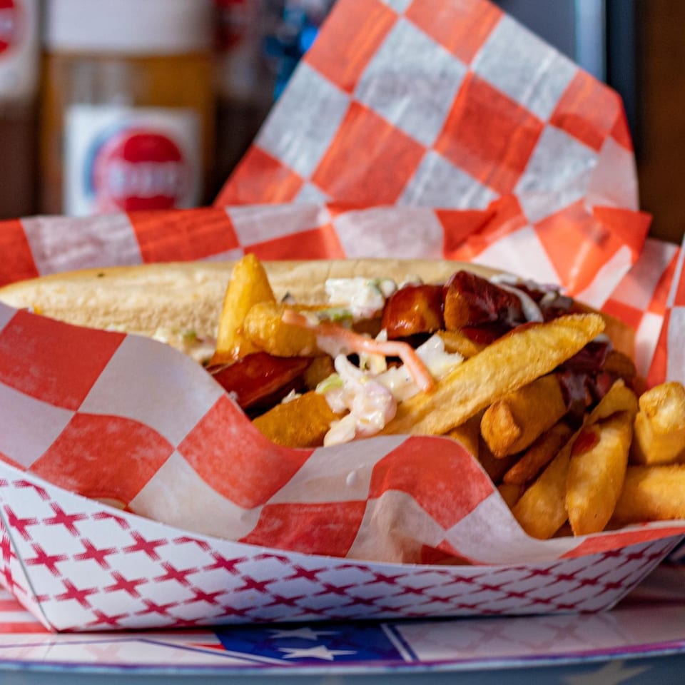 Real Smoq’ed BBQ’s hot dog with fries and coleslaw in a red and white checkered basket.