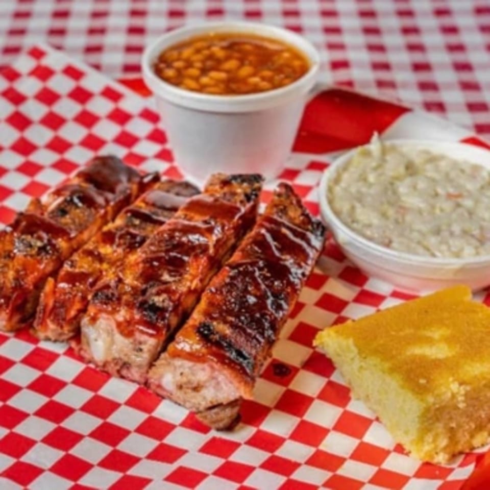 Real Smoq’ed BBQ ribs with baked beans, coleslaw, and cornbread on a red and white checkered paper.